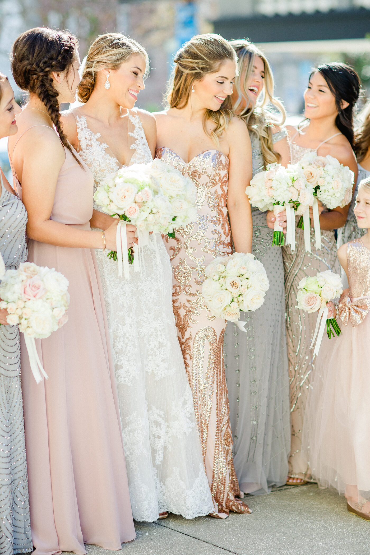 Bride in a rose gold embellished gown laughing with her bridesmaids in blush and silver, all holding white bouquets — Tampa Bay wedding photographer Ailyn La Torre