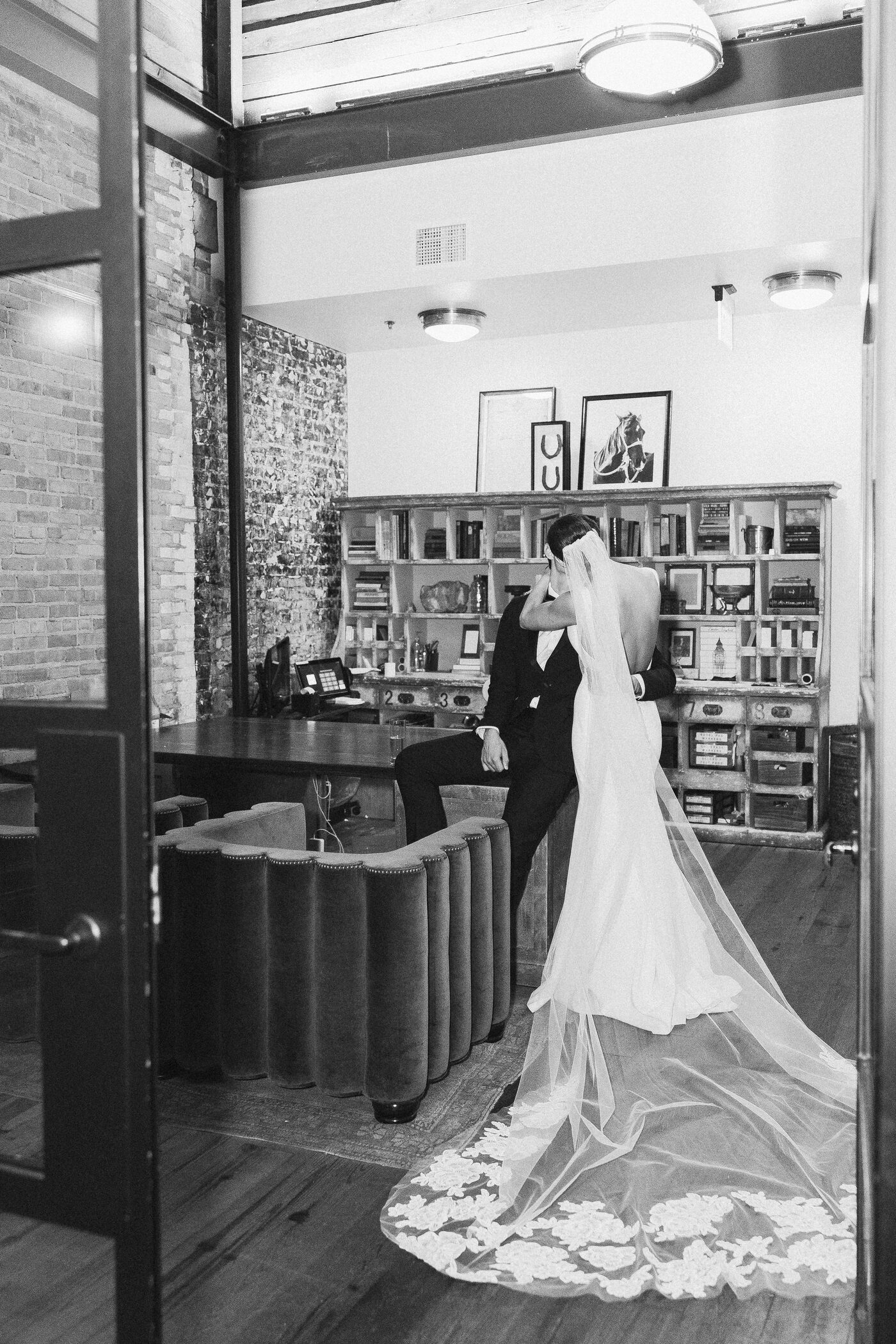 Bride and groom sharing a quiet kiss inside the Oxford Exchange in Tampa, bride's cathedral lace veil trailing dramatically across the floor — Tampa Bay wedding photographer Ailyn La Torre