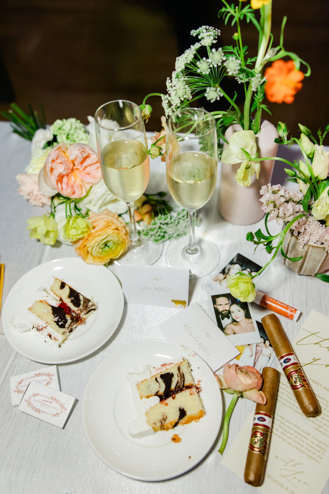Wedding reception table detail with champagne coupes, slices of cake, cigars, fresh florals, and polaroid photos — Tampa Bay wedding photographer Ailyn La Torre