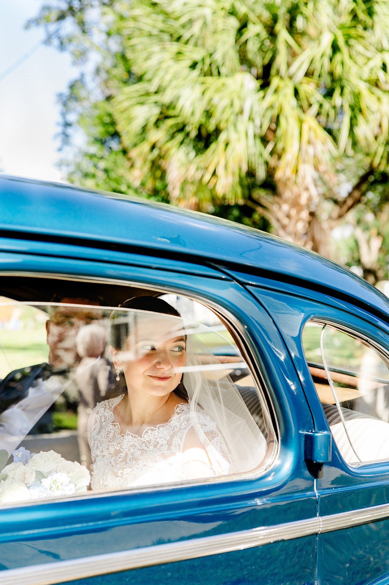 Bride gazing out through the window of a classic blue vintage car, lace veil and sunlight framing her face — luxury wedding photographer Ailyn La Torre
